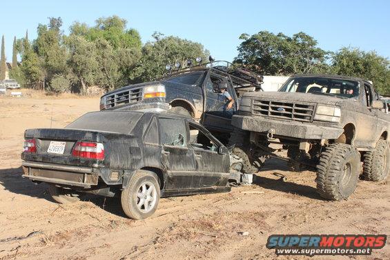 Three dirt-covered vehicles are crashed together in a dry, outdoor lot