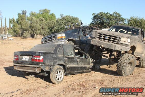 Three lifted trucks crush a sedan in a junkyard