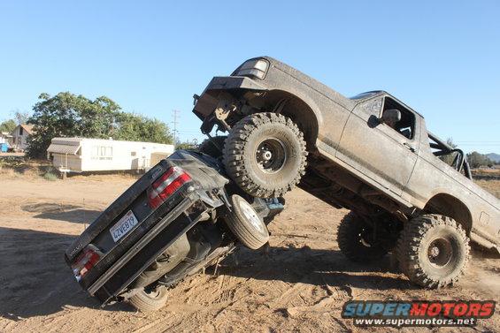 1992 Ford Bronco on top of a crushed car, off-roading