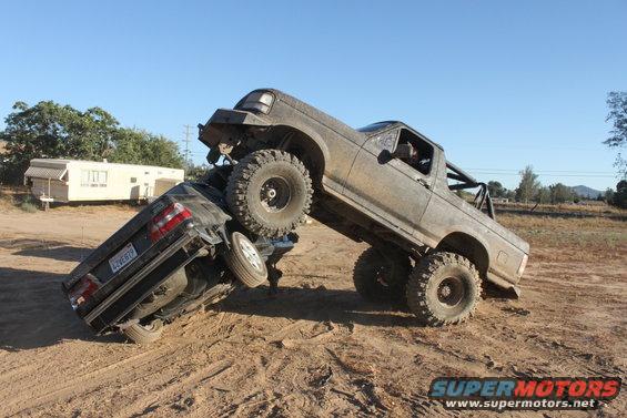 1992 Ford Bronco on top of a crushed car off-road