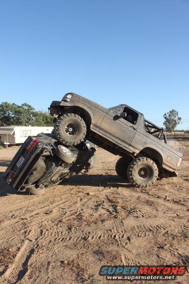 1992 Ford Bronco on top of another vehicle in a muddy off-road scene