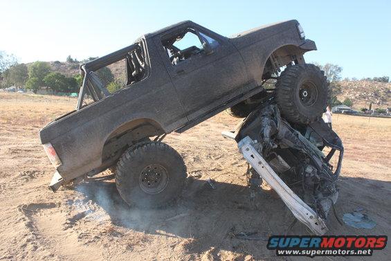 1992 Ford Bronco on top of a crushed vehicle in a dirt lot