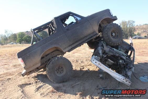 Black 1992 Ford Bronco crushing a car, lifted suspension, off-road tires