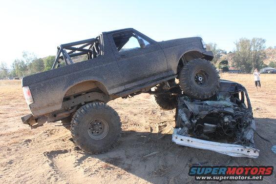 Modified 1992 Ford Bronco on top of a crushed car in a dirt lot