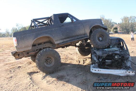 1992 Ford Bronco with roll cage on top of a crushed car, off-road tires