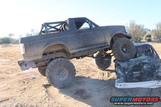 Modified 1992 Ford Bronco with roll cage on top of a crushed car