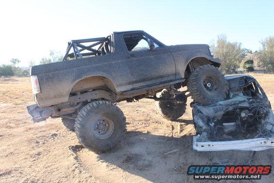 Modified SUV on top of a crushed car. The SUV has large off-road tires and a roll cage