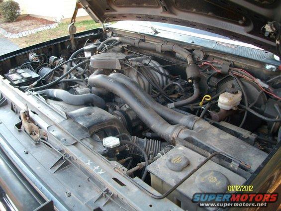 1990 Ford Bronco engine bay with hoses, battery, and fluids visible