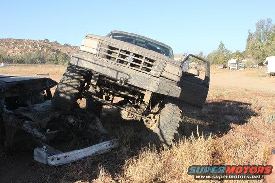 Lifted Ford truck on top of a wrecked car, driver's door open