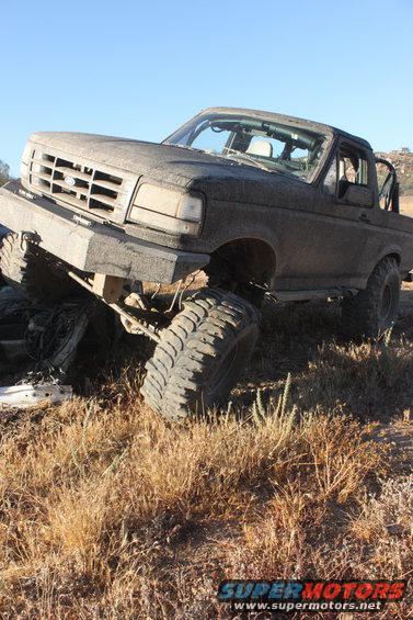 Mud-covered 1992 Ford Bronco with lifted suspension and large tires, tilted on its side