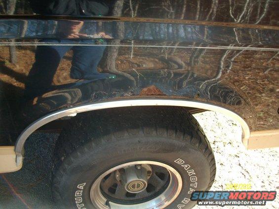 Black SUV fender with rust near wheel well and chrome trim