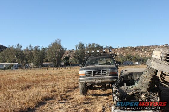 front view of a dark truck with a roof rack, next to a wrecked vehicle