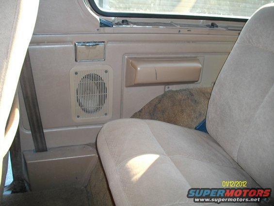 Interior door panel with speaker grille and armrest, rear seat visible