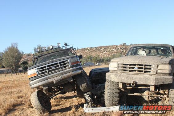 Two 1992 Ford Broncos are stuck together in a dry, grassy field under a clear blue sky