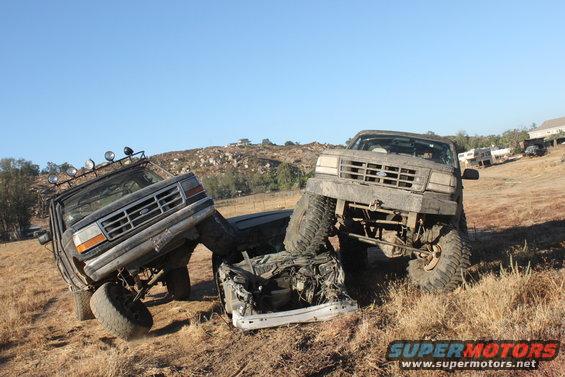 1992 Ford Bronco and another truck crushed together on a dry, grassy hill