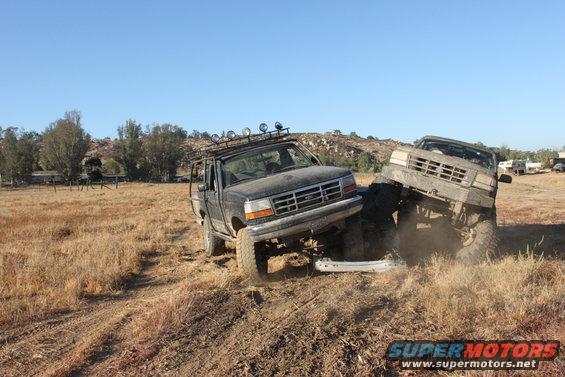 Two lifted trucks in a field, one on top of the other