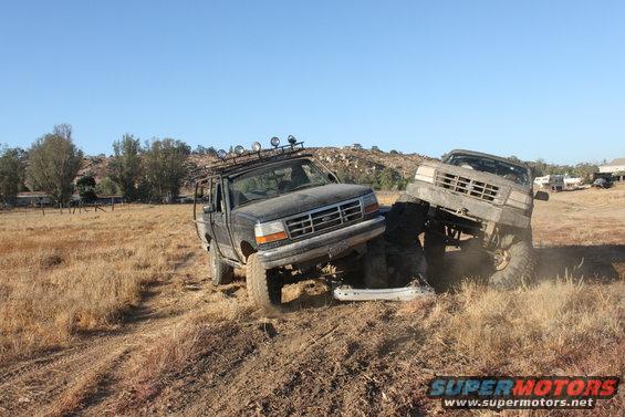 Two modified trucks stuck in a dirt embankment, one with a roof rack