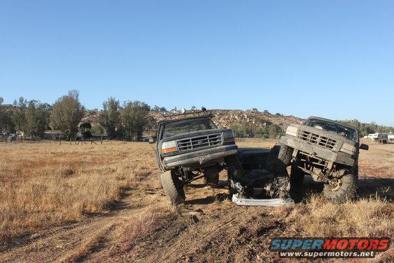 Two trucks are stuck in a field, one on top of the other, with damage
