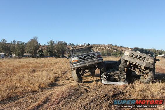 Two trucks are stuck on each other in a dry field. One truck is on top of the other