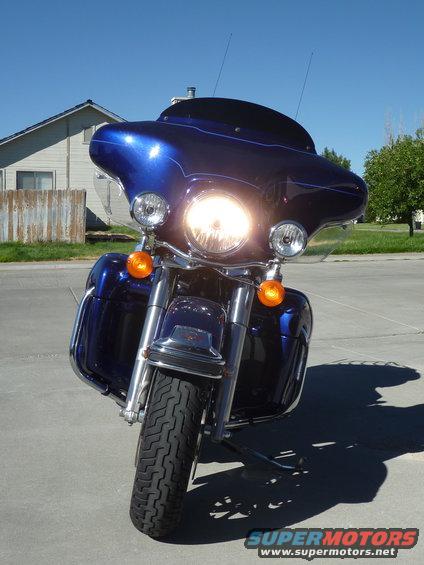 Front view of a blue motorcycle parked on pavement, with a house and fence in the background