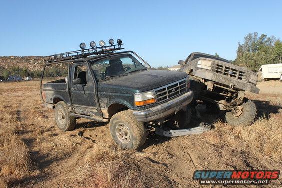 1992 Ford Bronco and another truck stuck in dirt, both with off-road modifications
