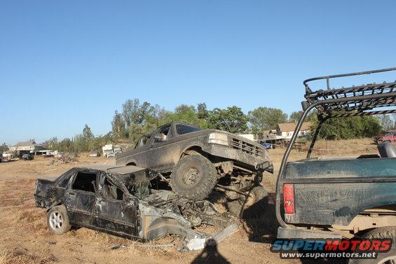 Mud-covered 1992 Ford Bronco on top of a crushed black sedan, front view