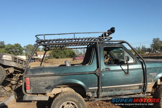 Green Ford Bronco with roll cage and roof rack, another vehicle in front