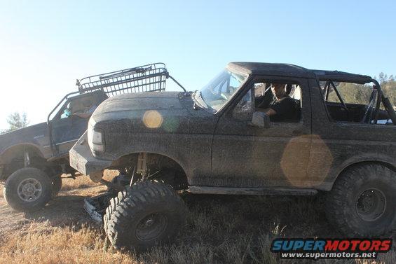 1992 Ford Bronco and another lifted SUV parked on dry grass
