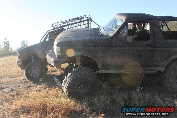 1992 Ford Bronco, mud-covered, lifted, with roof rack, parked next to another off-road vehicle