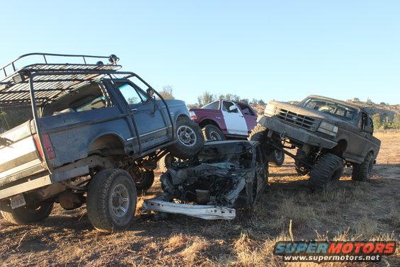 Three lifted trucks are stacked on top of each other in a field