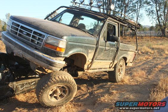Green pickup truck with off-road lights and roll cage, front-left tire on another vehicle