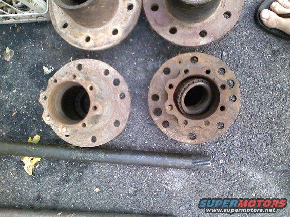 Four rusty wheel hubs and a metal shaft laid out on the ground