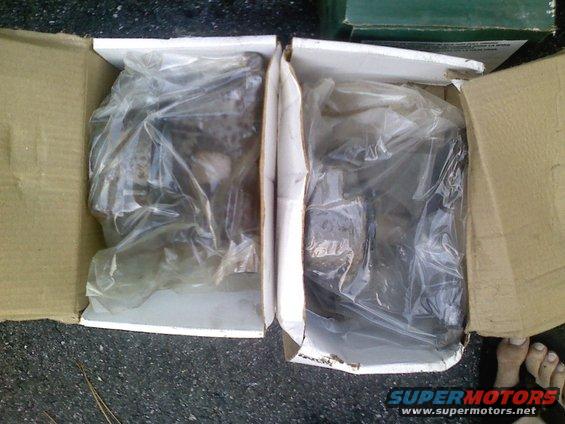 two boxes with plastic-wrapped car parts inside