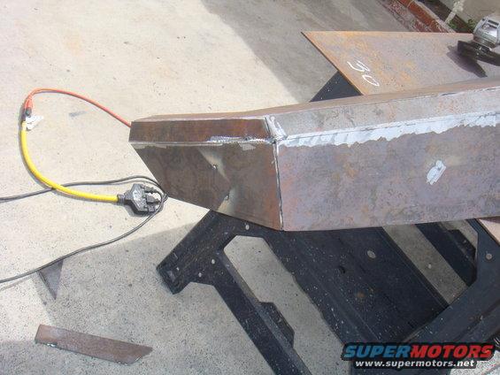 Welded steel bumper section on sawhorses, with power cord and grinder nearby