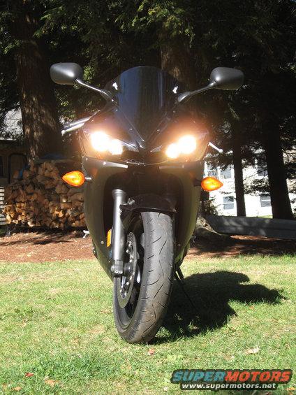 Black motorcycle front view with headlights on, parked on grass