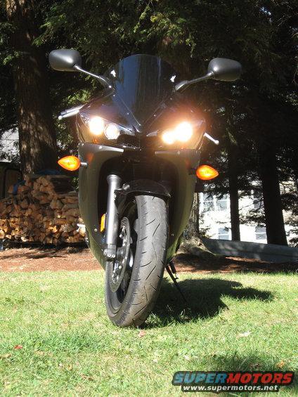 Front view of a black motorcycle parked on grass with headlights on