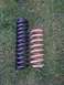 1992 Ford Bronco - Comparison of two coil springs, one new and black, the other old and rusted, resting on a grassy surface.