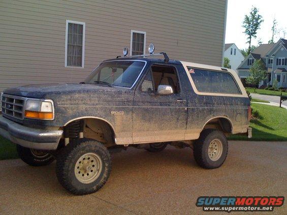1992 Ford Bronco, dark blue with tan top, covered in mud, lifted suspension, roof-mounted lights