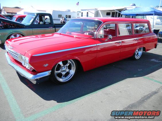 Red 1962 Chevrolet Nomad station wagon with custom chrome wheels parked next to a dark green pickup truck