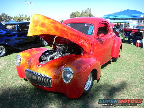 Red coupe with flame paint, hood open, showing engine. Chrome grille and headlights