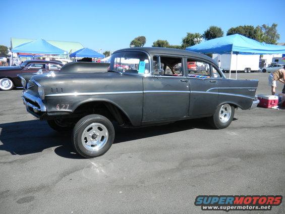 Dark gray 1957 Chevrolet Bel Air with a hood scoop and "427" emblem, seen from the front-right at a car show