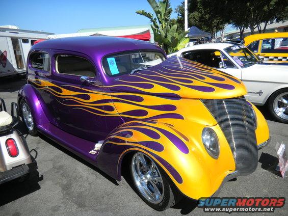 Purple and yellow hot rod with flame graphics parked next to a white car