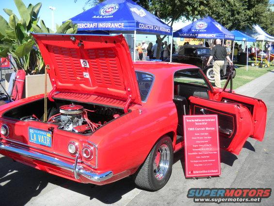 Red 1965 Corvair Monza with hood and doors open, showing engine and interior. Sign details car specs
