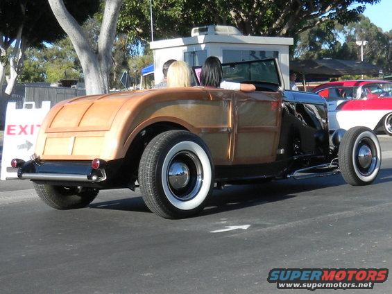 Woodie hot rod with whitewall tires and chrome hubcaps, seen from the rear quarter angle