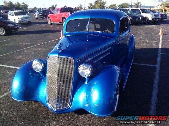 Blue hot rod coupe with chrome grille and headlights, parked in a lot