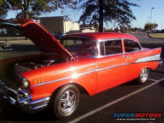 Orange 1957 Chevrolet Bel Air sedan with hood open, parked in a lot