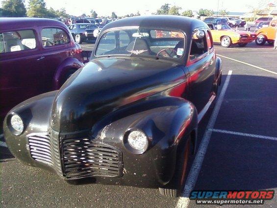 Black vintage car with a prominent grille and rounded fenders parked in a lot