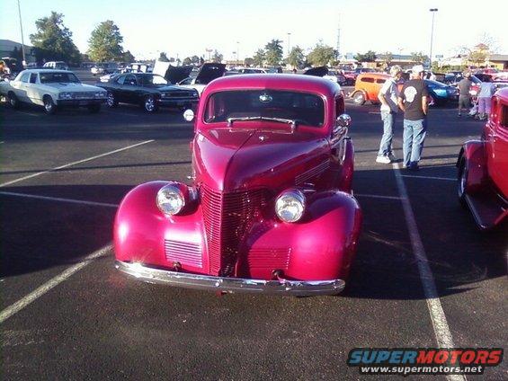 Front view of a shiny red vintage coupe at a car show