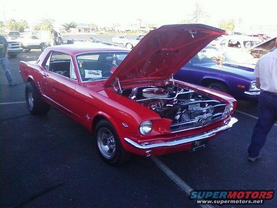 Red classic Ford Mustang coupe with hood open, showing engine. Another car is parked behind it