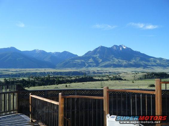 View of mountains from a wooden deck. Some snow on peaks. Blue sky